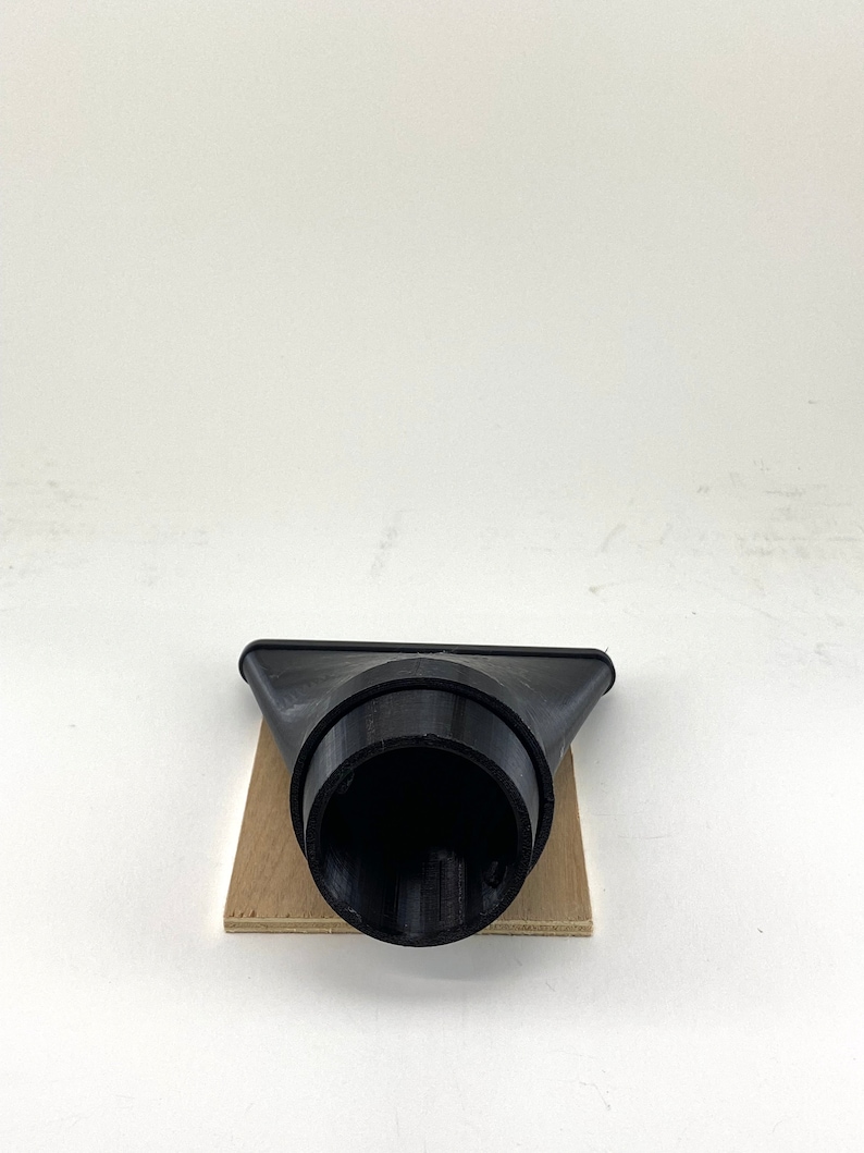 Puede incluir: Boquilla de recolecci&oacute;n de polvo de pl&aacute;stico negro con una abertura redonda. La boquilla est&aacute; sentada sobre un trozo de madera.