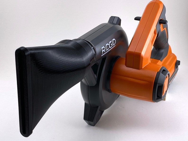 Puede incluir: Un soplador de hojas inal&aacute;mbrico negro y naranja con una boquilla larga. El soplador tiene la palabra "RIDGID" impresa en el lateral.