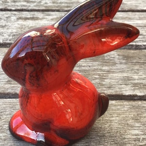 May include: A red and black glazed ceramic rabbit figurine. The rabbit is sitting up with its ears perked up.