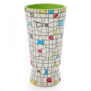 May include: A tall, ceramic vase with a white background and a grid pattern of black lines. The grid is interspersed with colorful squares of red, blue, yellow, and black. The interior rim is green.