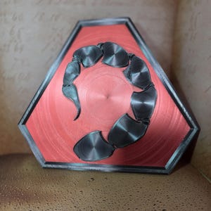 Könnte beinhalten: Ein rotes sechseckiges Schild mit einem schwarzen Skorpion-Design. Der Skorpion ist zu einem Kreis geformt.