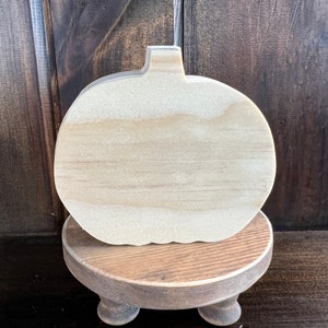 May include: A wooden pumpkin cutout on a wooden pedestal with three legs. The pumpkin is unfinished and ready to be painted or decorated.
