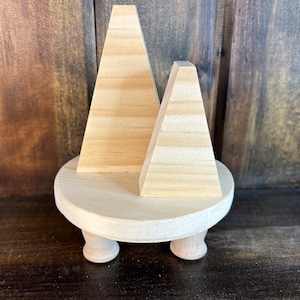 May include: A wooden stand with three legs, featuring two triangular wooden shapes resembling trees. The stand and shapes are a natural wood color.