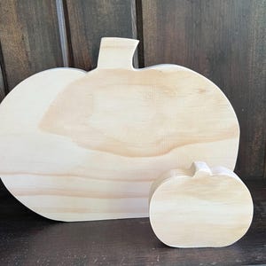 May include: Two unfinished wooden pumpkin cutouts. One is large and flat, the other is smaller and three-dimensional. Both have a light wood grain and are ready for painting or decorating. Perfect for fall crafts and seasonal decor.