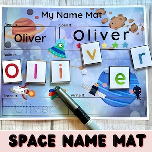 Pode incluir: Um tapete de aprendizagem de nomes com tema espacial com fundo azul, branco e cinza. O tapete apresenta um foguete, um planeta e um alienígena de desenho animado. O nome "Oliver" está impresso na parte superior do tapete, e as letras "O", "l", "i", "v", "e" e "r" estão impressas em peças individuais. O tapete também inclui um espaço para traçar o nome e um espaço para escrever o nome.