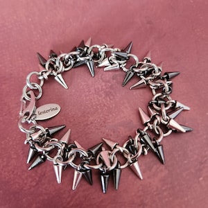 May include: A silver and black chain bracelet with multiple pointed spikes. The bracelet has a small tag that says "lesterina".