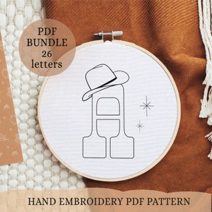 May include: A black and white line drawing of the letter A with a cowboy hat on top. The letter is in a hoop and there are two small stars to the right of the letter. The text "PDF BUNDLE 26 letters" is in the top left corner of the image. The text "HAND EMBROIDERY PDF PATTERN" is at the bottom of the image.