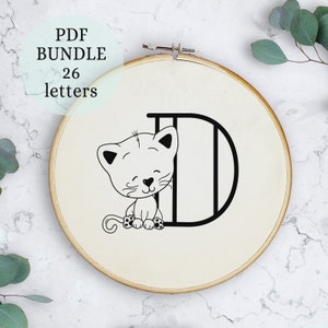 May include: A black and white embroidery design of a cat sitting inside the letter D. The design is on a white fabric background in a wooden embroidery hoop.