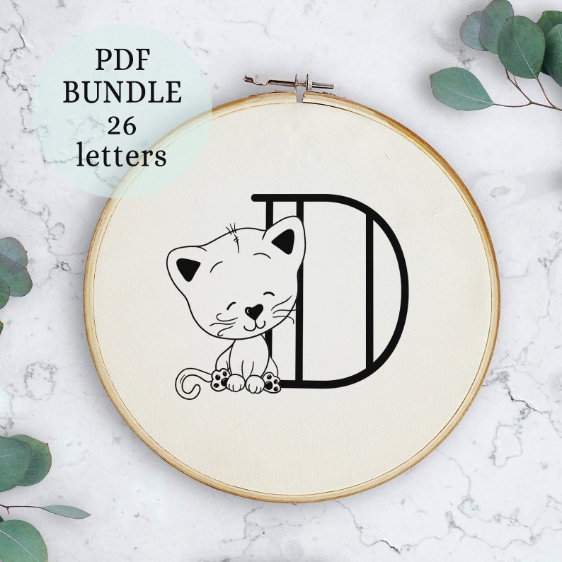 May include: A black and white embroidery design of a cat sitting inside the letter D. The design is on a white fabric background in a wooden embroidery hoop.