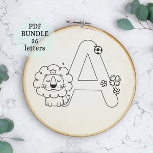 May include: A black and white embroidery hoop with a lion and the letter A. The letter A is outlined and has a soccer ball at the top. There are flowers around the letter. The lion is wearing a crown.