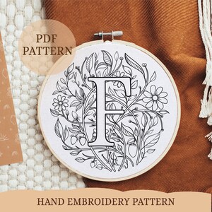 May include: A black and white hand embroidery pattern featuring the letter "F" surrounded by floral designs. The pattern is printed on a white background and is ready to be stitched.