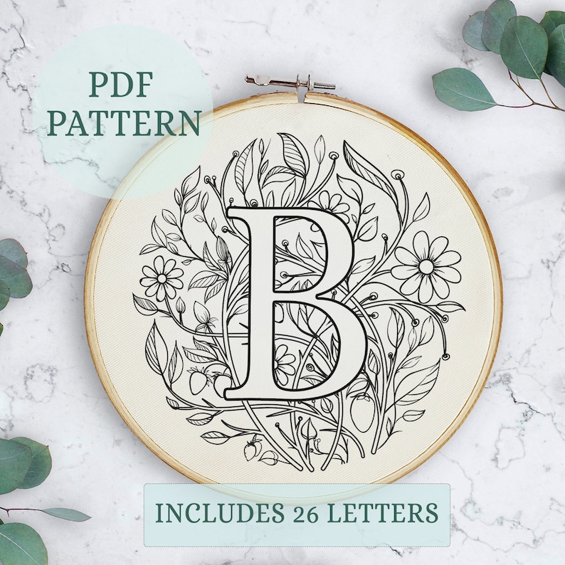 May include: Black and white embroidery pattern of the letter B surrounded by floral designs. The pattern is displayed in a round embroidery hoop. The text "PDF PATTERN" and "INCLUDES 26 LETTERS" is also included in the image.