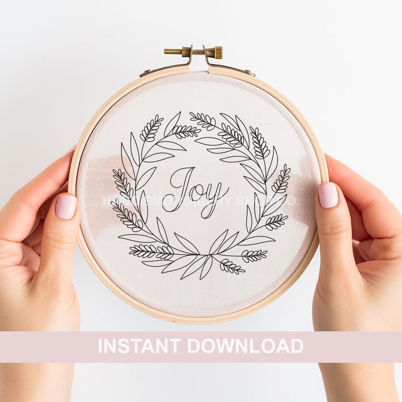 May include: A white embroidery hoop with a black line drawing of a wreath with the word "Joy" inside. The hoop is being held by two hands.