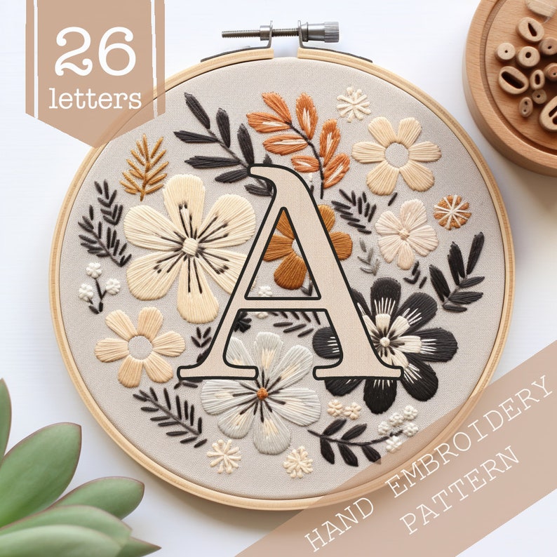 May include: A hand embroidery pattern featuring the letter A surrounded by floral designs in shades of beige, brown, and black. The pattern is displayed in a wooden embroidery hoop. The text "HAND EMBROIDERY PATTERN" is displayed at the bottom of the image.
