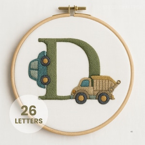 May include: Embroidered hoop art featuring a large green letter "D" with a blue car and a tan dump truck. The text "26 LETTERS" is in a white circle. The embroidery is set in a wooden hoop.