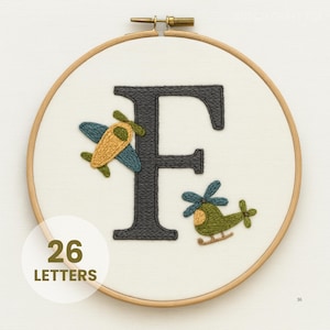 May include: Embroidered hoop art with a large, dark grey letter "F", a blue and yellow aeroplane, and a green helicopter. The text "26 LETTERS" is displayed. The design is set against a white background, within a wooden hoop.