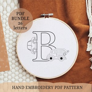 May include: A white embroidery hoop with a black outline of the letter B. A car and a dump truck are incorporated into the letter design. The text "PDF BUNDLE 26 letters" is in a white box with a black outline.