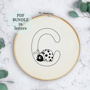Könnte beinhalten: Ein schwarzer und weißer Stickrahmen mit dem Buchstaben C und einem Marienkäfer darin. Der Rahmen befindet sich auf einer weißen Marmorfläche. Der Text "PDF BUNDLE 26 letters" befindet sich in einem schwarzen Kreis über dem Rahmen.