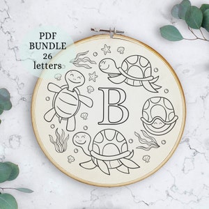 May include: A black and white embroidery hoop with the letter B surrounded by four turtles. The turtles have smiling faces and are surrounded by seaweed, seashells, and stars.
