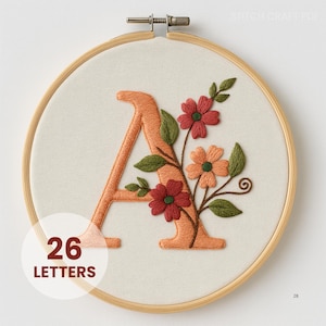 Peut inclure: Broderie du lettrage "A" orange, orné de fleurs rouges et oranges et de feuilles vertes, sur un tissu crème dans un cercle à broder en bois. Le texte "26 LETTERS" est affiché en bas.