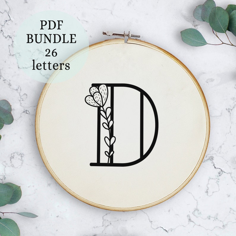 May include: A black and white embroidery pattern of the letter D with a floral design. The pattern is displayed in a wooden embroidery hoop.