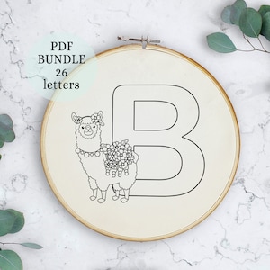 Puede incluir: Patrón de bordado en blanco y negro de una llama con una corona de flores y un collar de cuentas, de pie junto a la letra B. El patrón está sobre un fondo de tela blanca en un aro de bordado de madera.