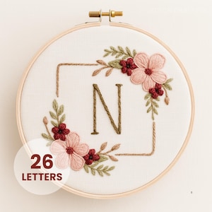 May include: Embroidered hoop art featuring the letter "N" in brown thread, surrounded by a floral design with pink and burgundy flowers and green leaves. The text "26 LETTERS" is in a white circle at the bottom.