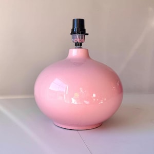 Può includere: Una lampada da tavolo in ceramica rosa con base rotonda e portalampada nero. La lampada ha una finitura lucida e un corpo sferico. La lampada è progettata per uso interno ed è un apparecchio di illuminazione decorativo.