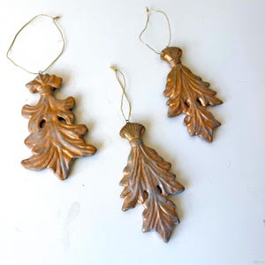 May include: A trio of cream-glazed ceramic mugs with a speckled finish. Each mug is adorned with a hand-painted design: a blue and green leaf, a yellow flower, and a red berry. The mugs have a simple, rounded form.