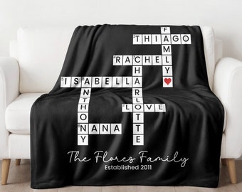 May include: Black fleece throw blanket with a crossword puzzle design featuring family names, including Thiago, Rachel, Isabella, Anthony, Harley, Love, and Nana. The text "The Flores Family Established 2011" is printed at the bottom.