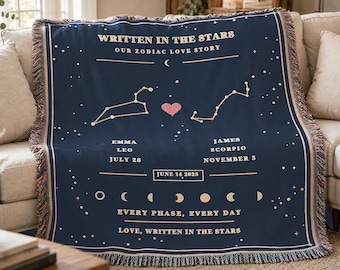 May include: A navy blue woven throw blanket featuring a celestial design with the text WRITTEN IN THE STARS, OUR ZODIAC LOVE STORY, names Emma and James, zodiac signs Leo and Scorpio, dates, a pink heart, moon phases, and the text EVERY PHASE, EVERY DAY.