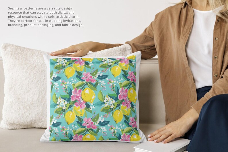 May include: A square decorative pillow with a vibrant floral pattern featuring yellow lemons, pink flowers, and green leaves on a turquoise background. The pillow is placed next to a white, textured pillow.
