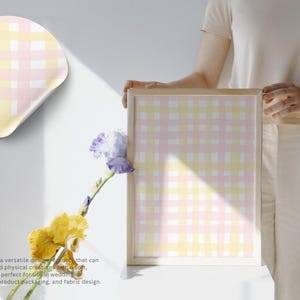 May include: A framed print and a sticker featuring a pastel pink, yellow, and white gingham pattern. The print is held by a person. The image also includes yellow and purple flowers.
