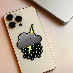 May include: A gray cloud with a yellow lightning bolt and black raindrops on a white iPhone case.