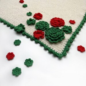 May include: A white crocheted tablecloth with a green crocheted border. The tablecloth is decorated with red and green crocheted flowers.
