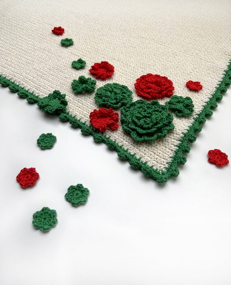 May include: A white crocheted tablecloth with a green crocheted border. The tablecloth is decorated with red and green crocheted flowers.