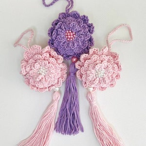 May include: Three crocheted flower ornaments with pink and purple tassels. The flowers are pink and purple and have a beaded center.