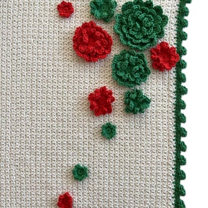 May include: A white crocheted blanket with a green border and red and green crocheted flowers.