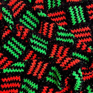 May include: Close-up of a crocheted textile with a repeating pattern. The design features vibrant neon green and red zigzags set against a black background. The texture appears soft and handmade, with a slightly irregular stitch.