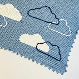 May include: A blue crocheted baby blanket with a white crocheted cloud design. The blanket has a scalloped edge.