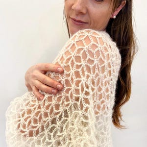 Könnte beinhalten: Ein weißer Häkel-Schal mit einem zarten Blumenmuster. Der Schal ist leicht und luftig, perfekt zum Überziehen über ein Kleid oder eine Bluse.