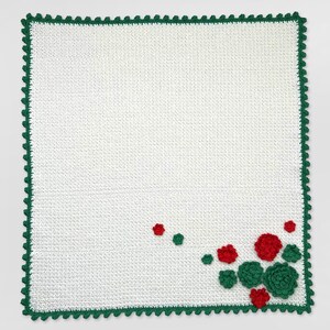 May include: White crocheted blanket with a green crocheted border and red and green flower embellishments in the corner.