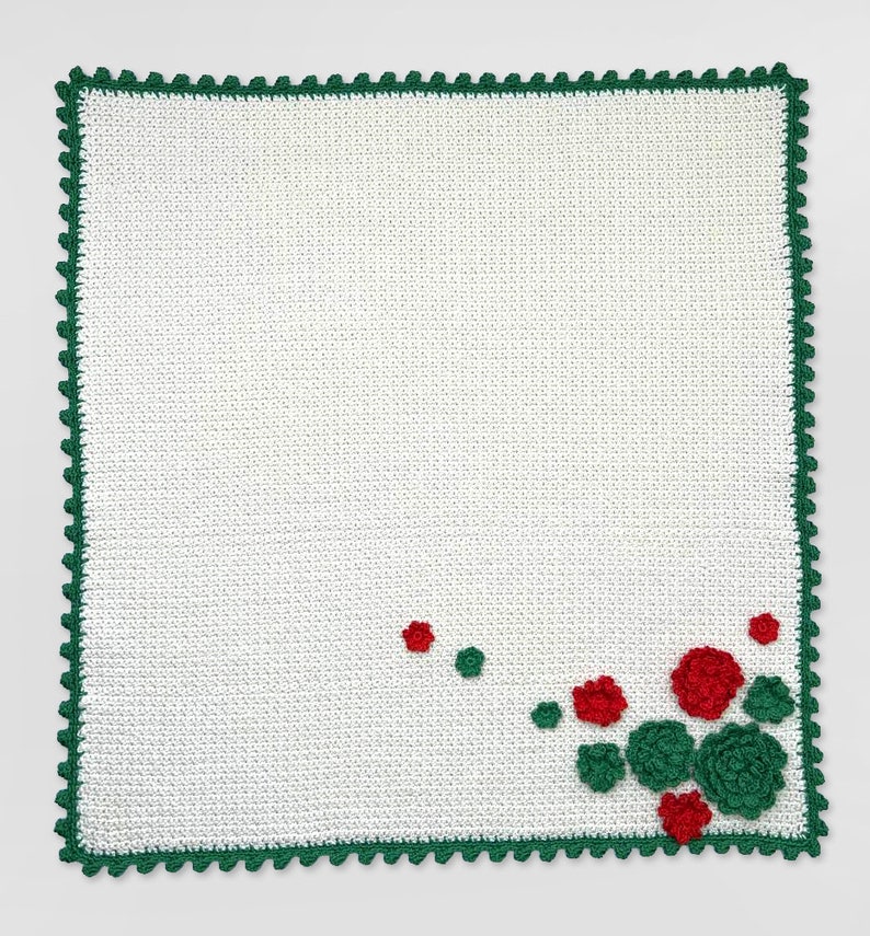 May include: White crocheted blanket with a green crocheted border and red and green flower embellishments in the corner.