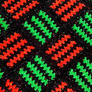 May include: Close-up of a crocheted textile with a repeating pattern. The design features rows of bright red and neon green zigzags set against a black background. The black yarn has flecks of other colors.