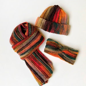 May include: A set of three crocheted accessories in a multi-colored striped pattern. The set includes a beanie, a headband, and a scarf, all in shades of brown, orange, red, and green.