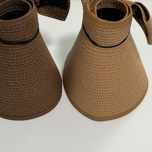 May include: Two brown straw sun hats with black trim. The hats have a wide brim and a chin strap.