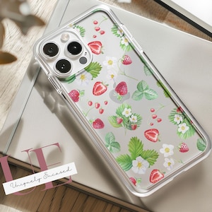 Puede incluir: Funda transparente para teléfono con un diseño de fresas. La funda presenta un diseño repetido de fresas rojas, flores blancas y hojas verdes. El texto "Uniquely Encased" está impreso en una etiqueta blanca.