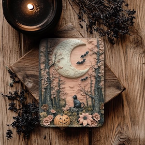 May include: A rectangular Halloween-themed decorative plaque featuring a crescent moon, bats, trees, a black cat, and a jack-o'-lantern. The plaque is set against a pinkish background with floral accents. A lit black candle and dried foliage are in the background.