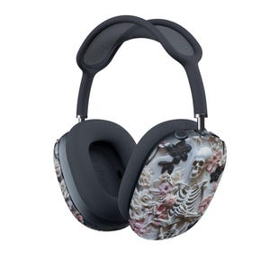 May include: Over-ear headphones featuring a dark gray headband and mesh ear cushions. The outer ear cups display a detailed graphic print of a white human skeleton intertwined with various pink, white, and black floral blossoms against a light background.