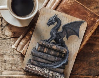 May include: A black dragon figurine with outstretched wings sits atop a stack of antique-looking books. The dragon is detailed with textured scales. The base has the text "Name or Phrase here". A cup of coffee sits in the upper left corner.
